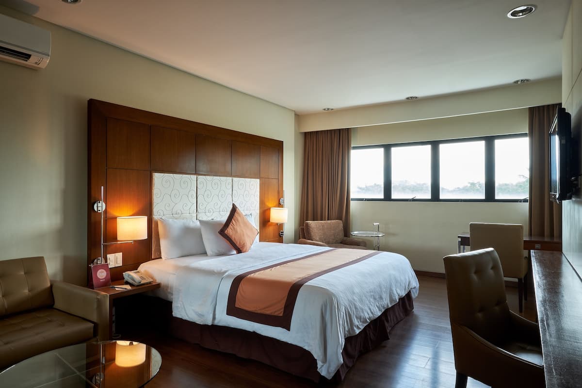 A hotel room with a large bed, bedside tables, a desk, and a TV.