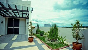 Une terrasse sur le toit agrémentée de plantes en pot, une pergola et une façade d’immeuble moderne.