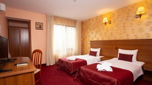 Une chambre d’hôtel avec deux lits, un bureau, une chaise, une télévision et une fenêtre avec des rideaux.