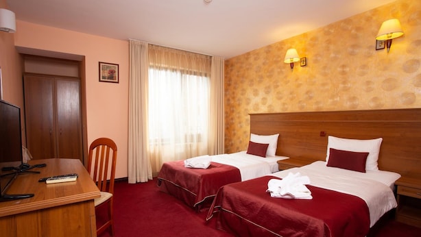 Een hotelkamer met twee bedden, een bureau, een stoel, een televisie en een raam met gordijnen.