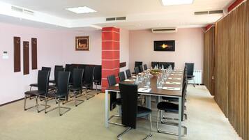 Un salón de conferencias con una larga mesa, sillas y una pared roja decorativa.