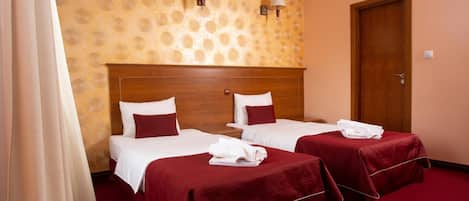 Habitación de hotel con dos camas, cada una con cubrecama rojo y ropa de cama blanca, cabeceros de madera y pared estampada.