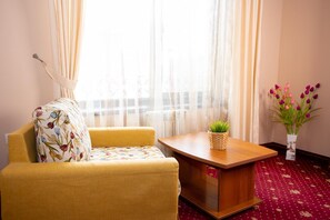A room with a yellow armchair, a small wooden table with a woven basket, and a vase with flowers.