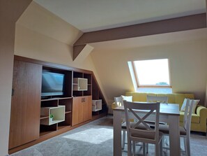 A room with a TV, wooden cabinets, a yellow sofa, and a dining table with chairs.