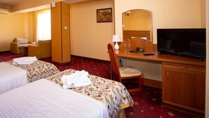 Une chambre d’hôtel avec deux lits, un bureau avec une télévision, une chaise et une petite table avec une lampe.