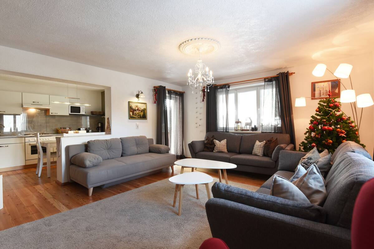 Una sala de estar moderna con un sofá gris, una mesa de centro blanca y un comedor con una cocina al fondo.