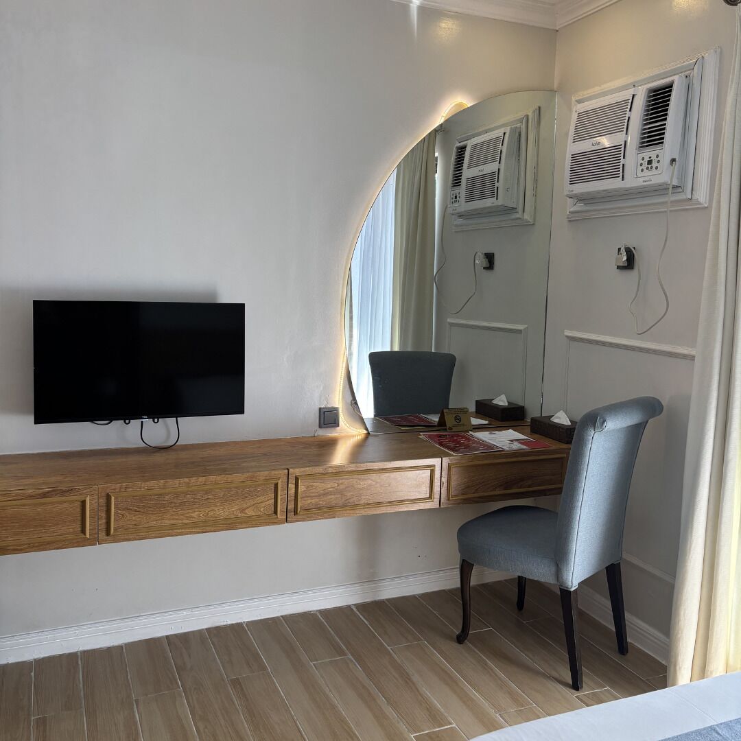 A modern room with a flat-screen TV mounted on a wooden console, a large mirror, and an air conditioning unit on the wall.