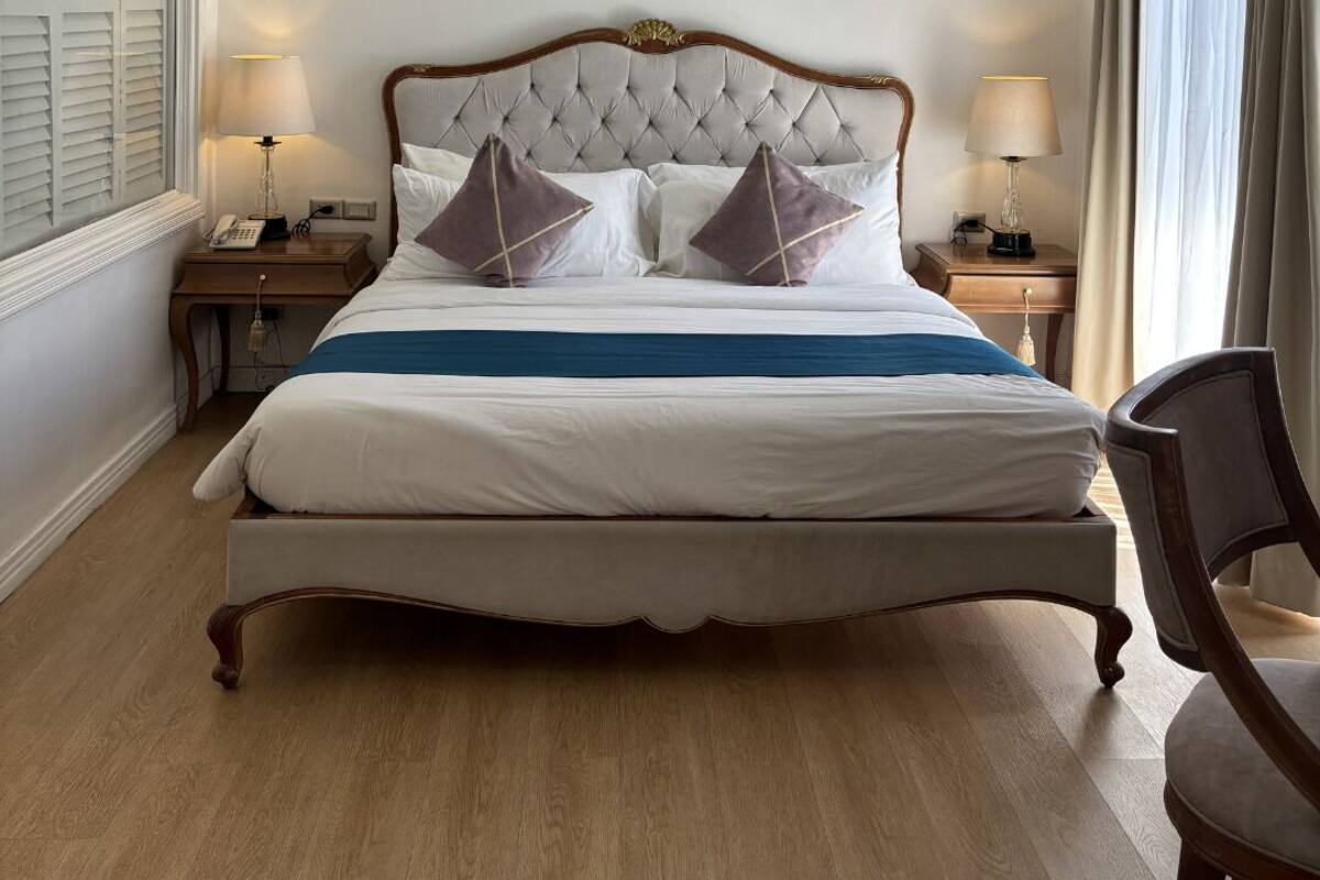 Een groot bed met een gestapeld hoofdbord, twee nachtkastjes met lampen, een stoel, en een uitzicht op het plafond en de wanden van de kamer.