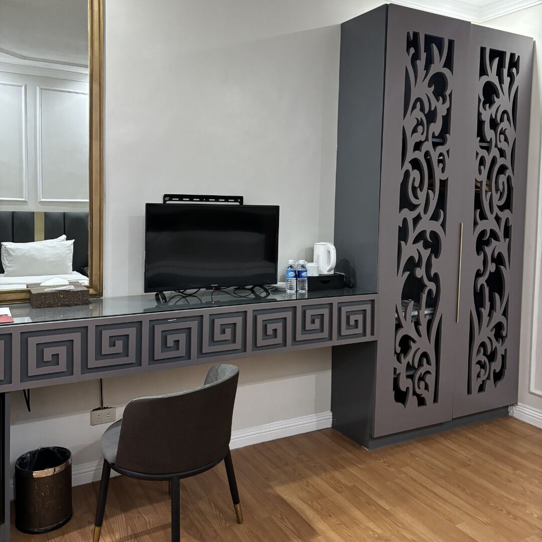 Une chambre d’hôtel équipée d’un bureau, d’une télévision, d’une chaise et d’une armoire ornée de panneaux décoratifs.