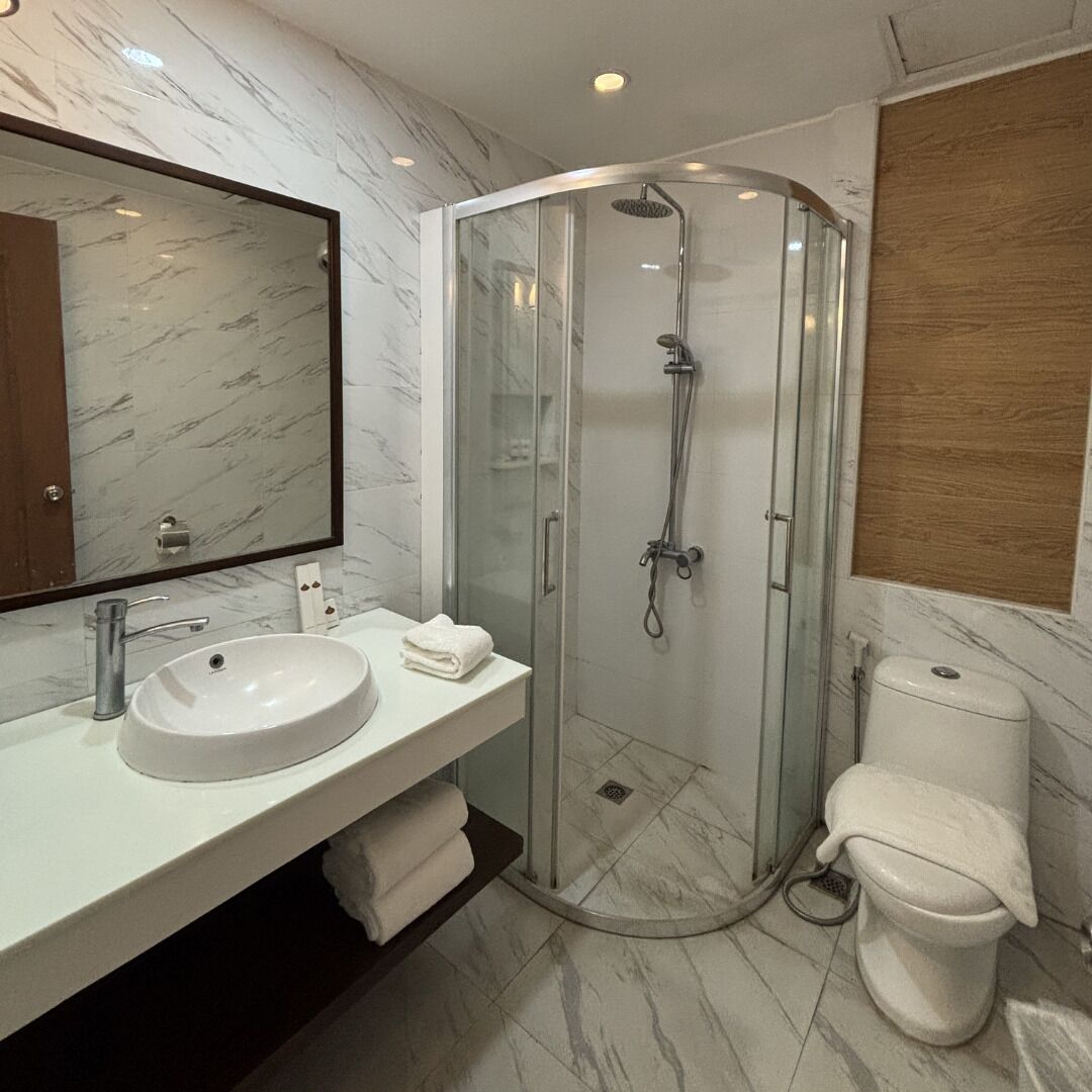 A modern bathroom with a glass-enclosed shower, a marble-tiled floor, a white sink, and a toilet.