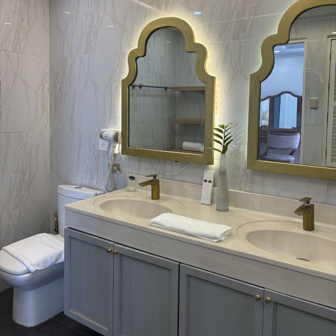 A modern bathroom with marble walls, a double sink vanity, a toilet, and a large mirror with an ornate frame.