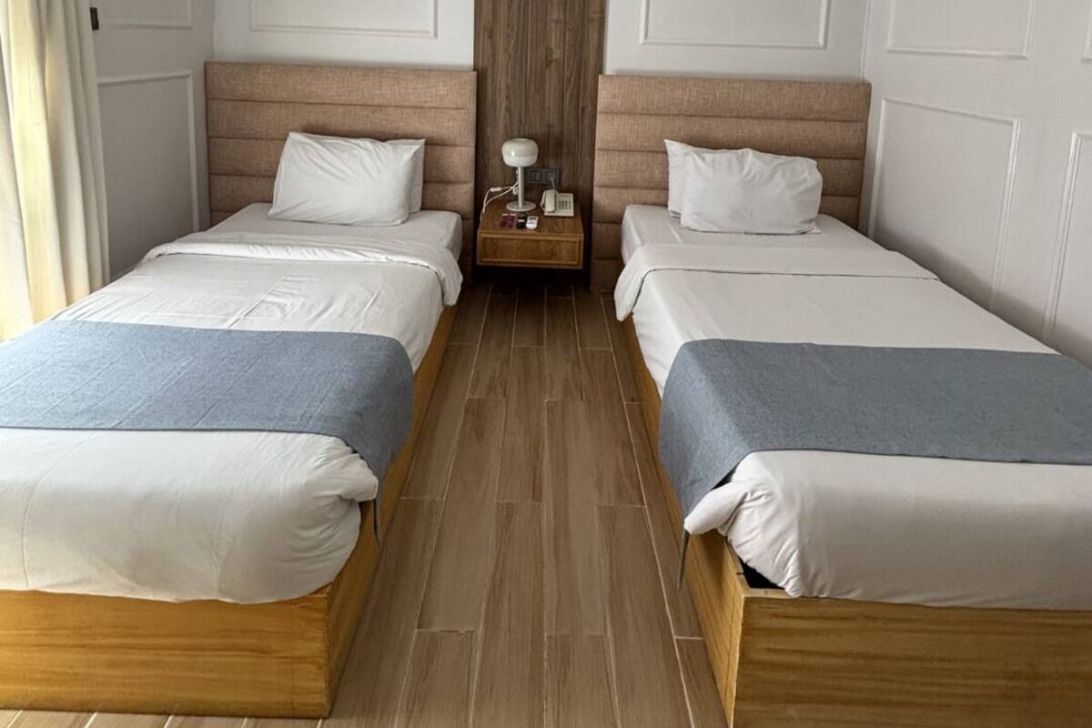 Een hotelkamer met twee enkele bedden, houten hoofdeinden, een nachtkastje met een lamp en een houten vloer.