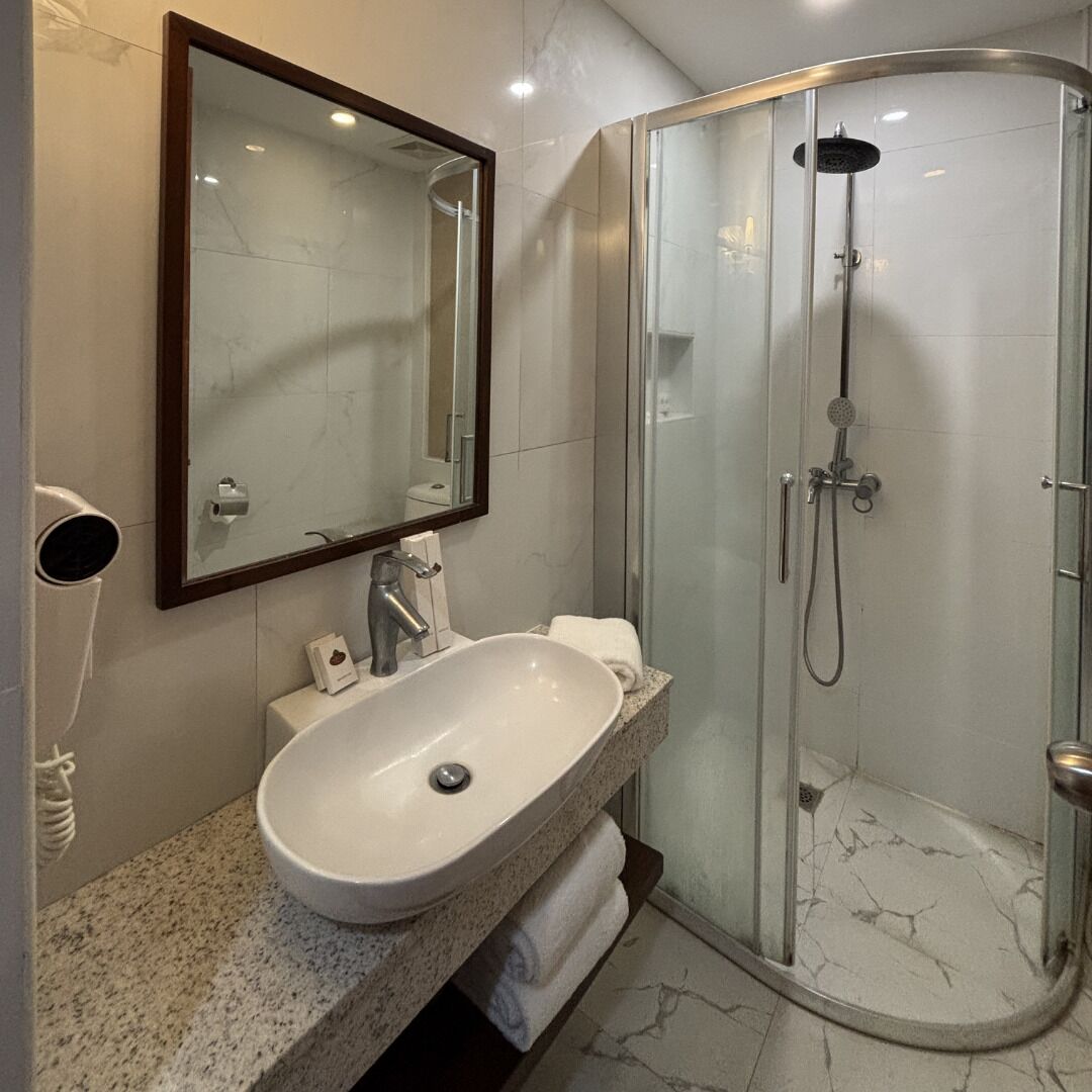 Un baño moderno con cabina de ducha curva, un espejo grande y una encimera de granito con lavabo.