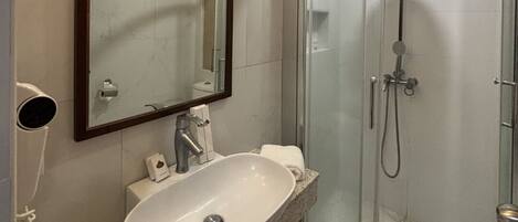 Un baño moderno con cabina de ducha curva, un espejo grande y una encimera de granito con lavabo.