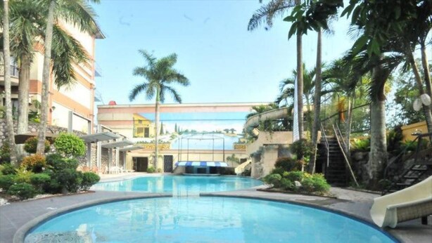A swimming pool surrounded by palm trees and a building with a blue and white facade. - Queen Margarette Hotel - Main (Lucena)