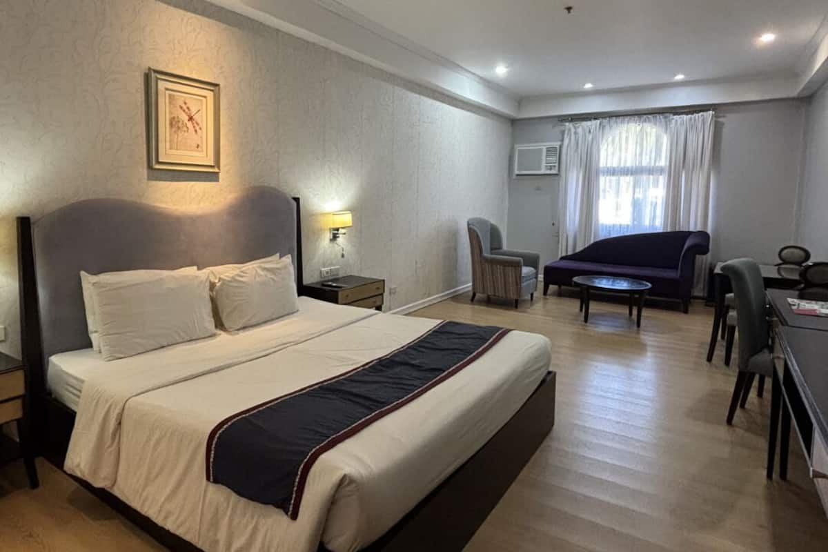 Hotelkamer met een groot bed, een bureau, een stoel, een bank en een raam met gordijnen.