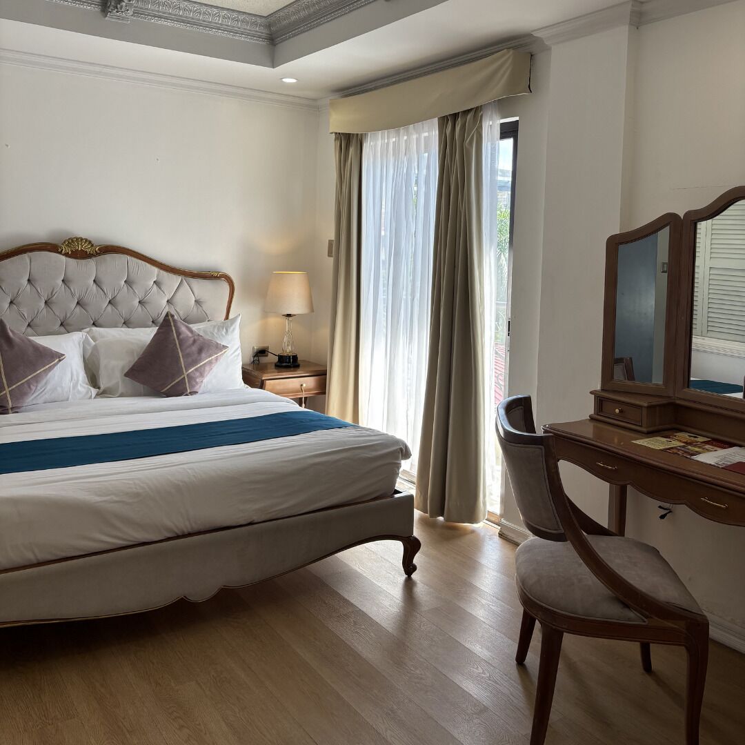 A hotel room with a large bed, a desk with a chair, a lamp, and a mirror.