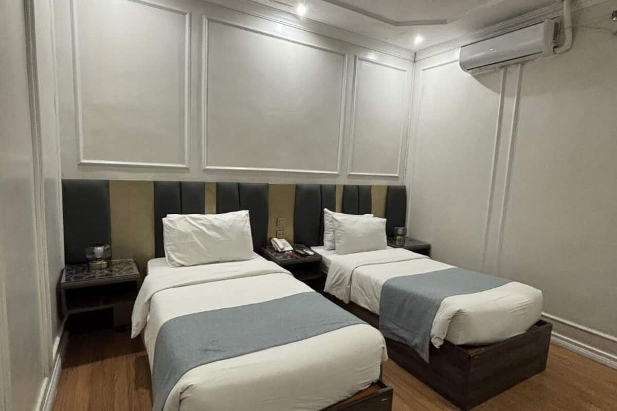 Een hotelkamer met twee bedden, een nachtkastje, een telefoon en een airconditioning.