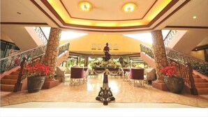 A spacious lobby with a high ceiling, a central statue, and multiple staircases leading to upper floors. - Queen Margarette Hotel - Main (Lucena)