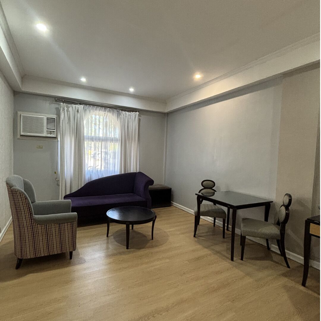 A living room with a purple sofa, a wicker chair, a small round table, and a dark wooden coffee table.