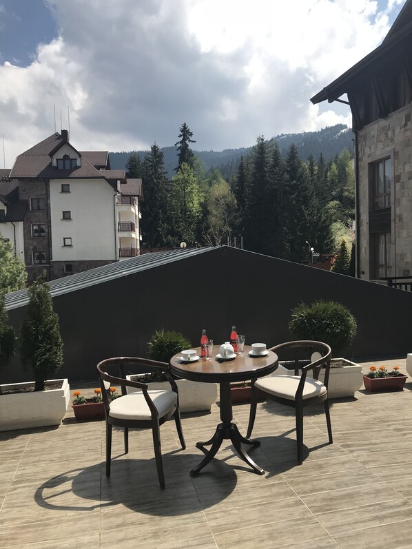 Une terrasse avec une table ronde et des chaises, entourée de plantes en pot et offrant une vue sur un paysage montagneux.