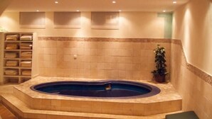 Uma área de spa com hidromassagem, paredes revestidas de azulejos e um armário com toalhas.
