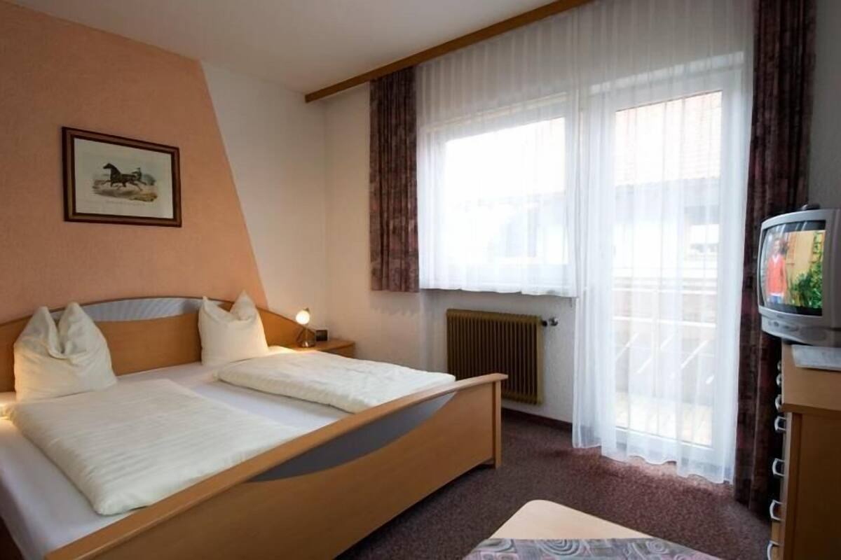 Een hotelkamer met een bed, een nachtkastje met lamp, een televisie en een raam met gordijnen.