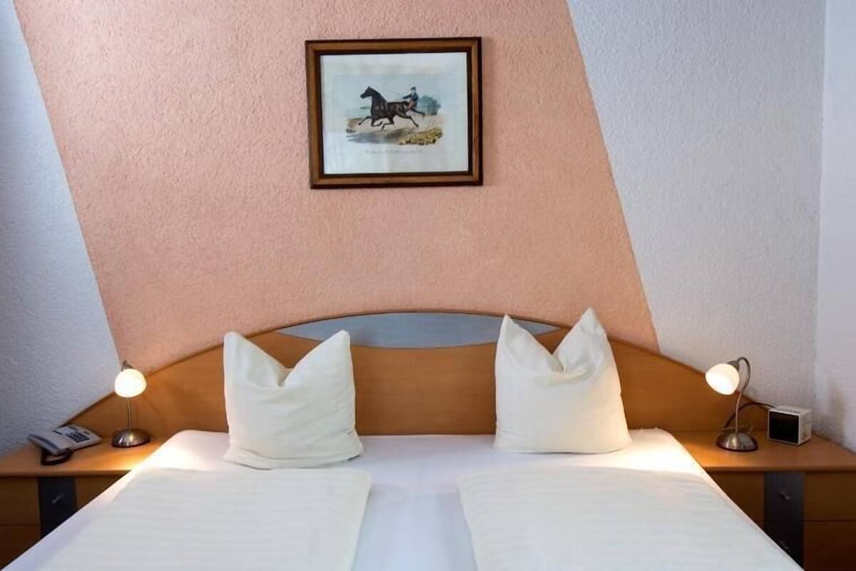 Een hotelkamer met een bed, twee bedlampen, een ingelijst schilderij aan de muur, en een tafeltje met een telefoon en een radio.