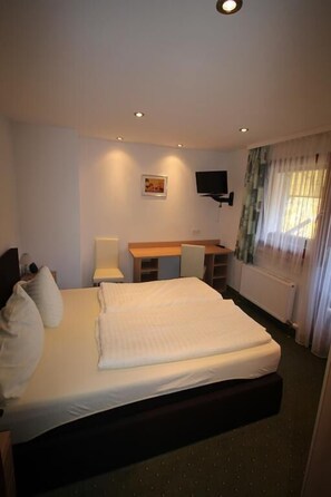 Ein Hotelzimmer mit einem großen Bett, einem Schreibtisch, einem Stuhl, einem Fernseher und einem Fenster mit Vorhängen.