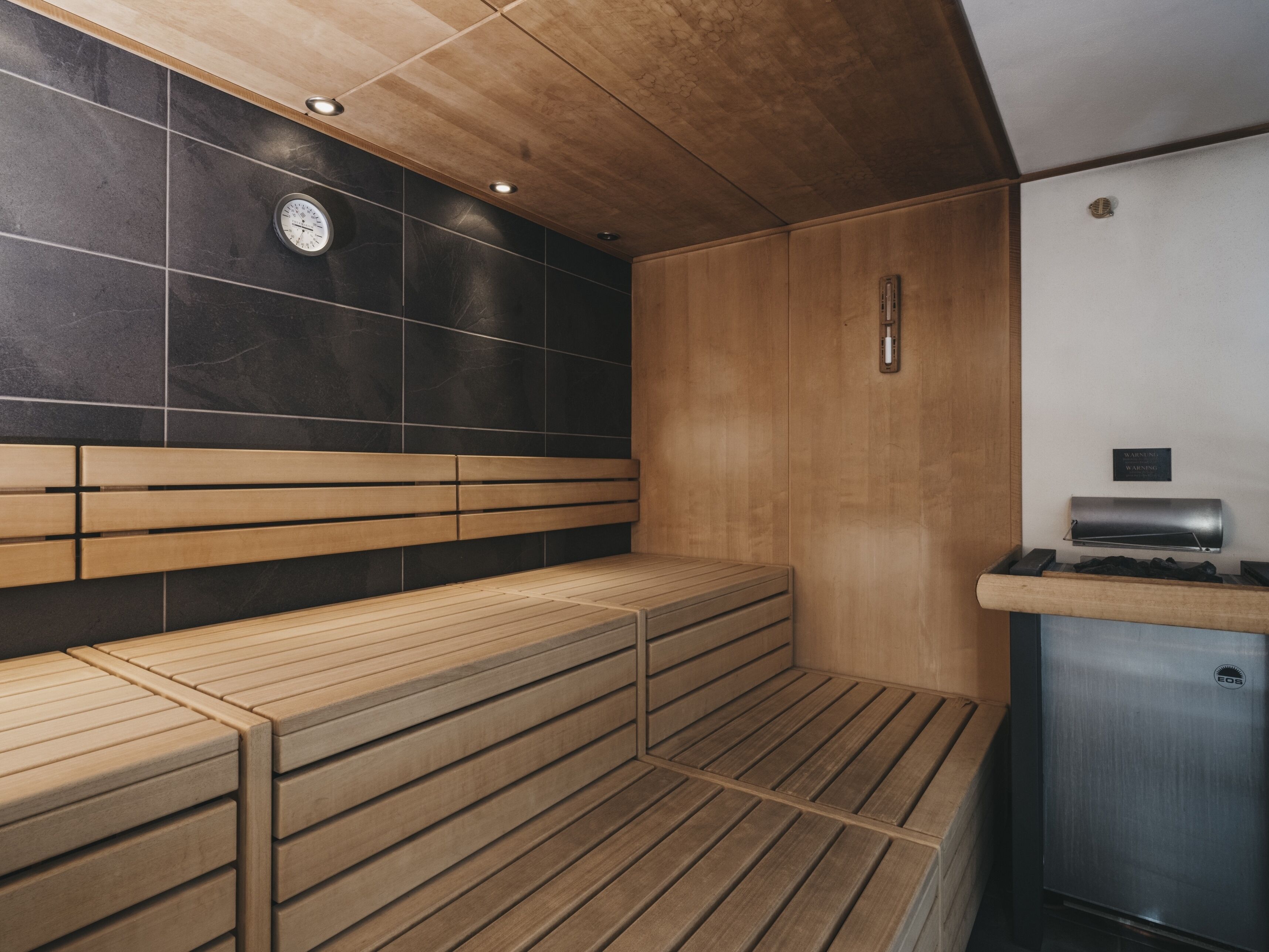 A sauna room with wooden benches, a wall-mounted heater, and a control panel.