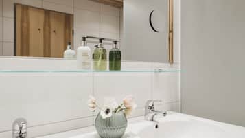 Un baño con techo de madera, un lavabo blanco, un espejo y una repisa con artículos de aseo.