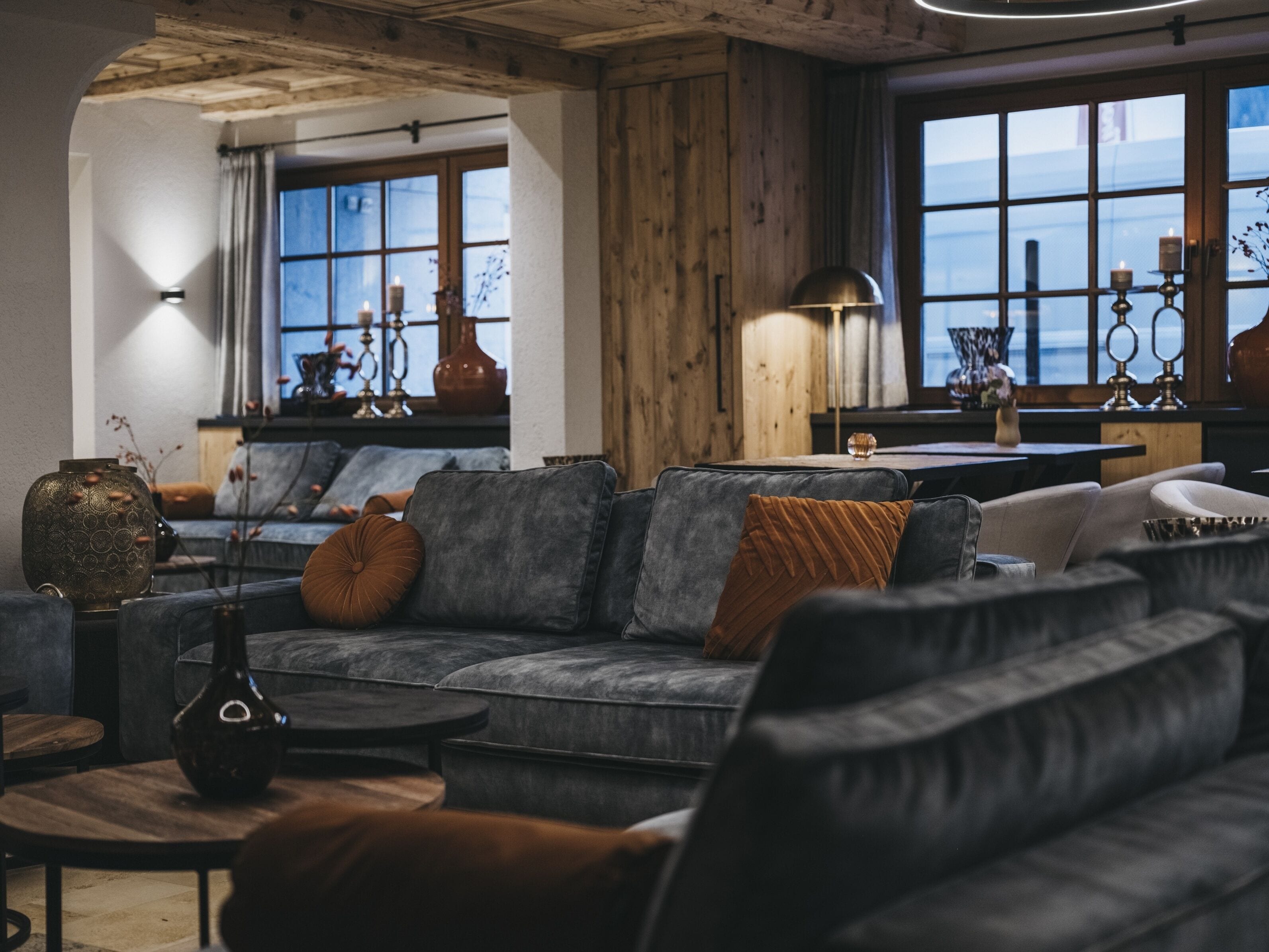 A modern living room with a grey sofa, wooden accents, and a view of the sea through large windows.