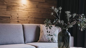A modern living room with a wooden wall, grey sofa, and a round coffee table with a vase of dried flowers and a plate of fruit.