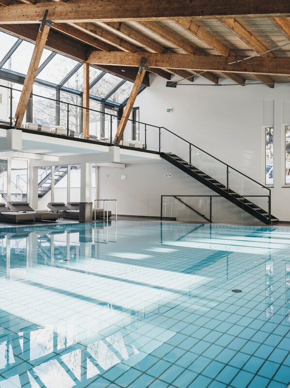 Una piscina interior con suelo de cristal, vigas de madera y una escalera que lleva a un balcón.