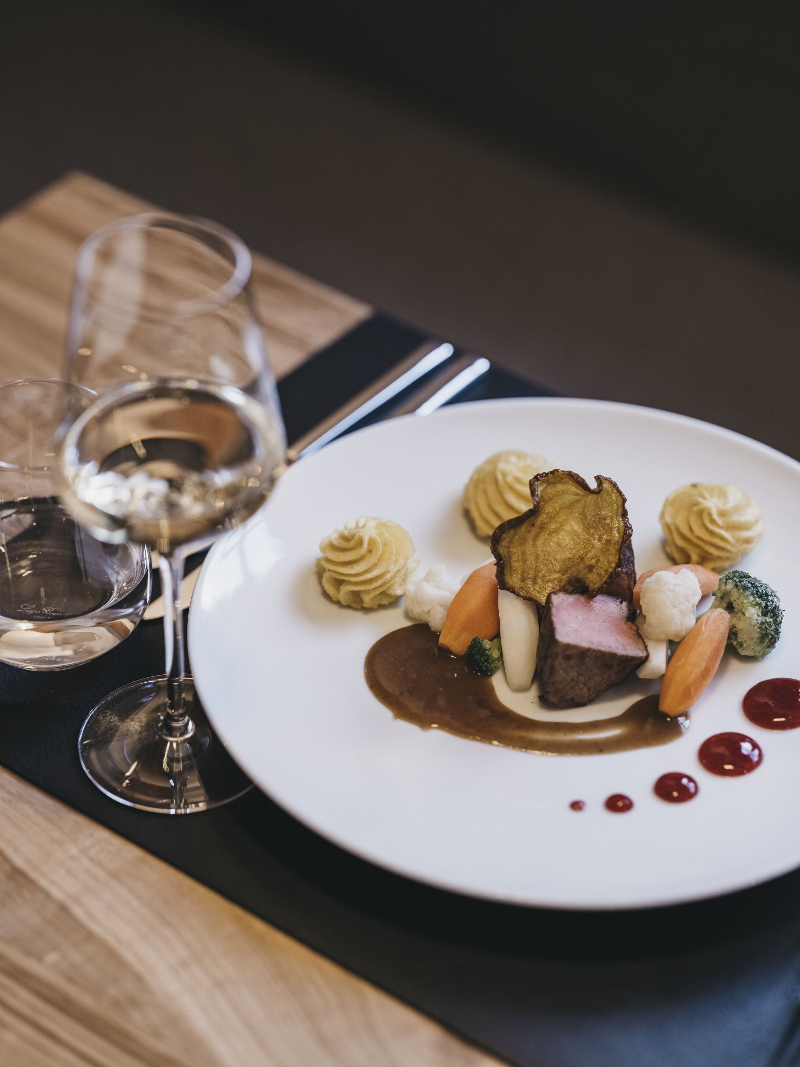 Ein weißer Teller mit verschiedenen Speisen, darunter Fleisch, Gemüse und Soße.