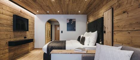 A modern bedroom with wooden paneling, a bed, a grey sofa, and a flat-screen TV mounted on the wall.