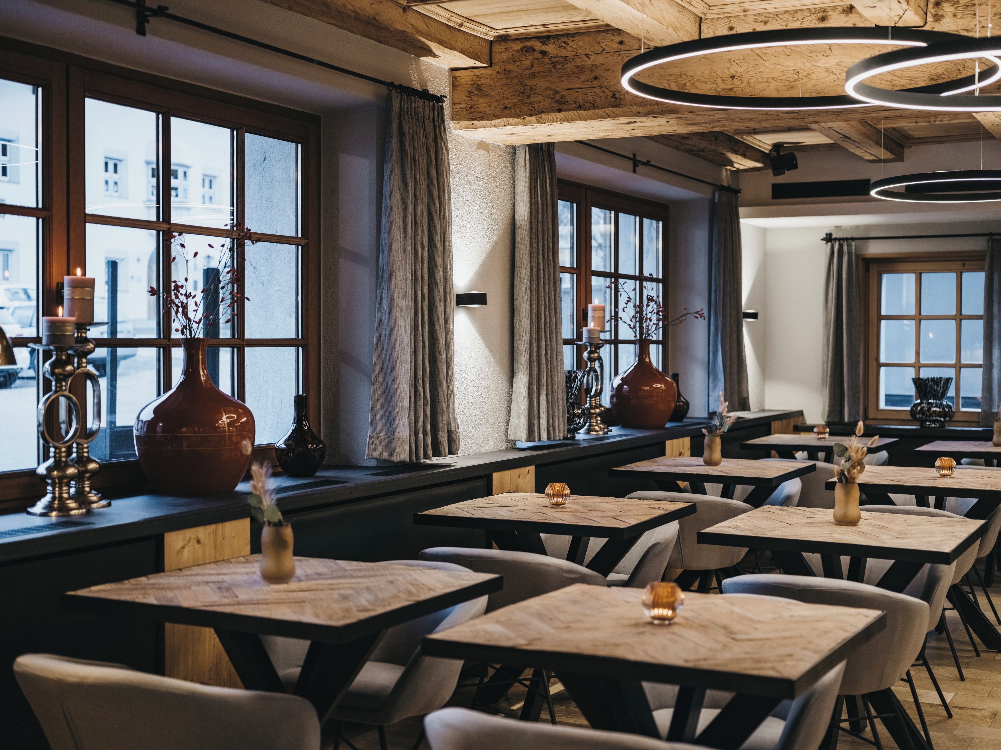 Ein Restaurantinnenraum mit mehreren Tischen, Stühlen und Kerzen auf den Fensterbänken.