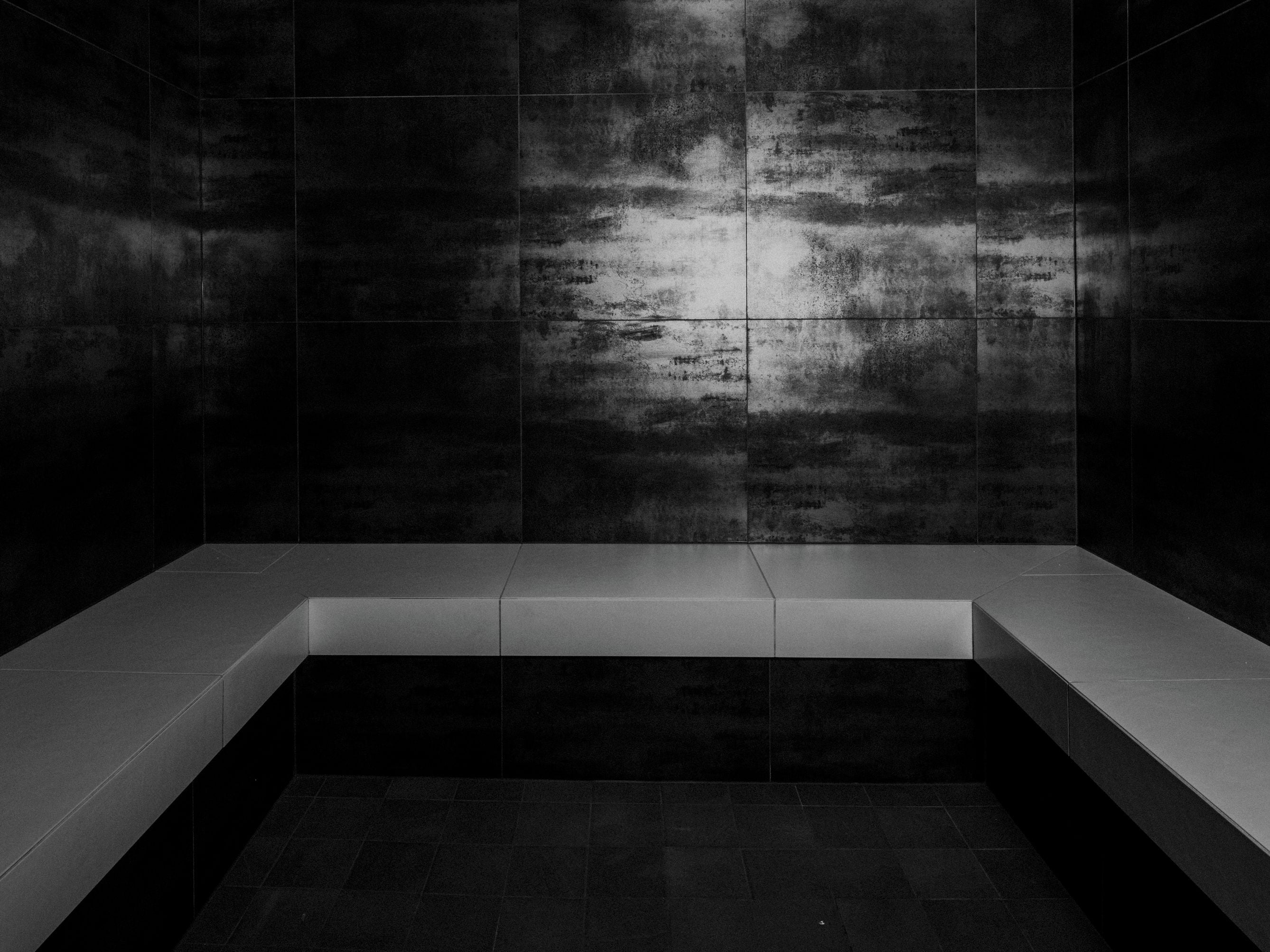 A modern, minimalist bathroom with a dark tiled wall and a white bathtub.