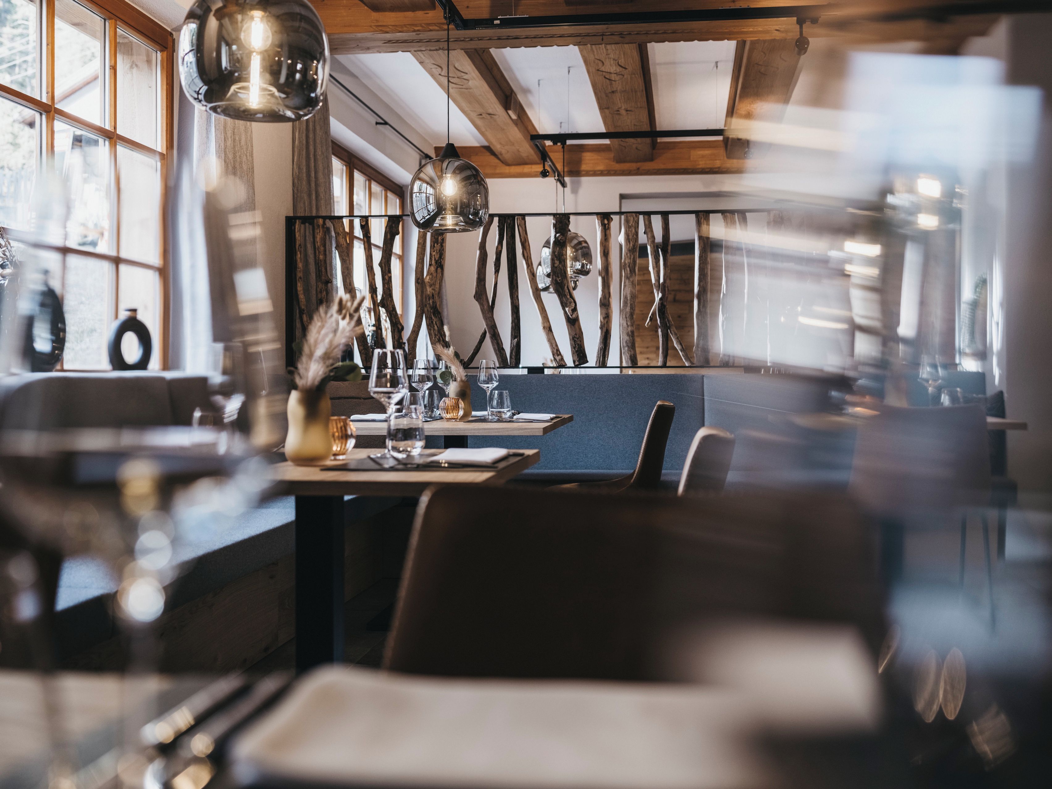 A restaurant interior with wooden beams, hanging pendant lights, and a dining area with tables and chairs.