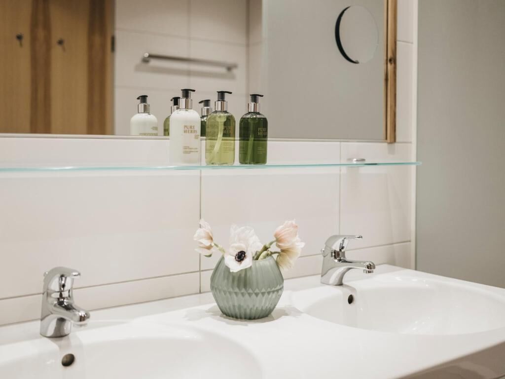 A bathroom with a glass shelf holding toiletries, a vase with flowers, and a mirror.