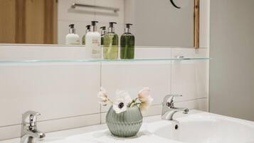 A bathroom with a glass shelf holding toiletries, a vase with flowers, and a mirror.