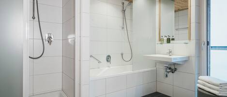 A modern bathroom with white tiles, a wooden ceiling, a bathtub, a shower, and a sink with a mirror above it.