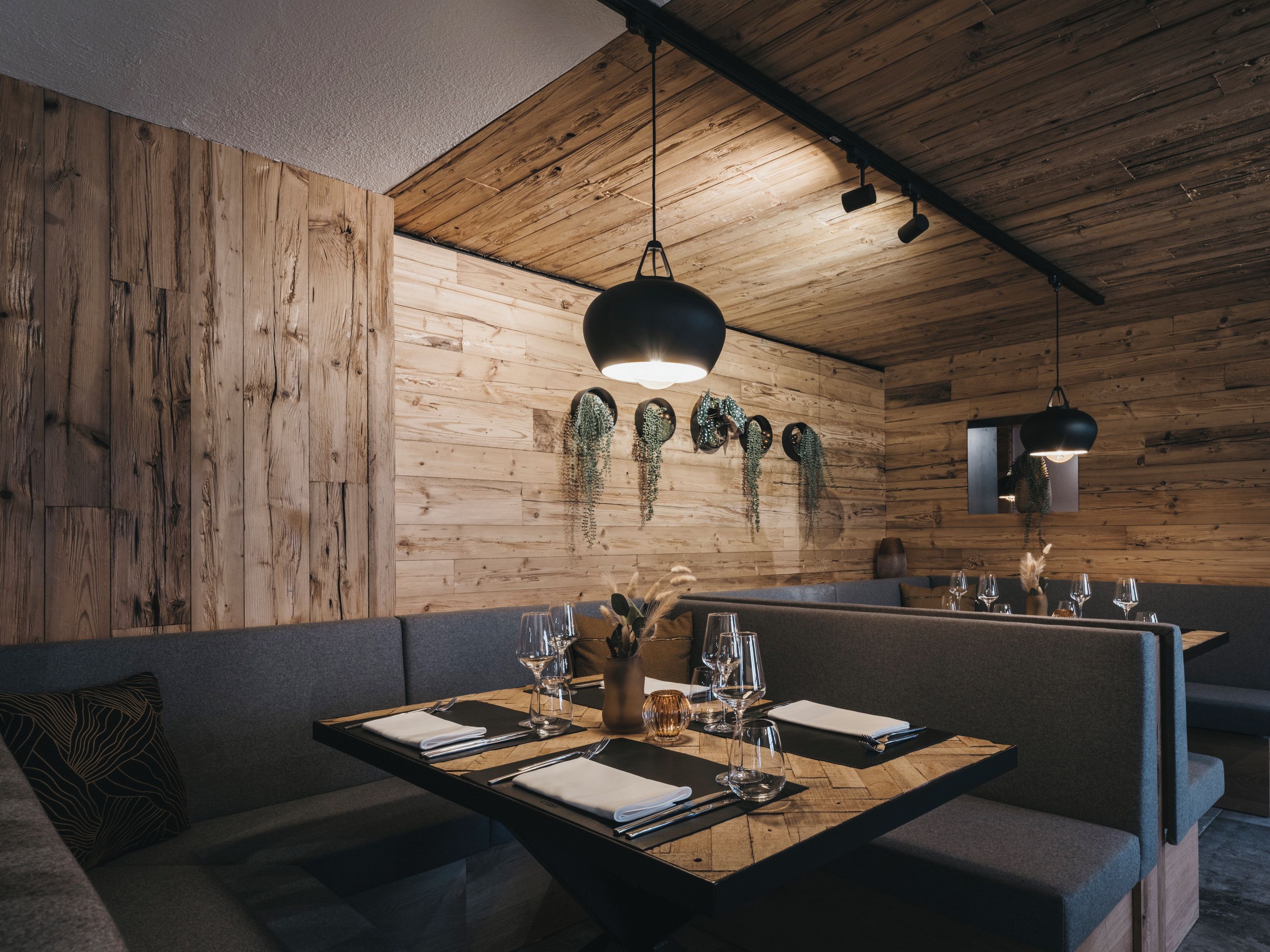 A wooden interior with a dining table set for four, a sofa, and hanging plants.