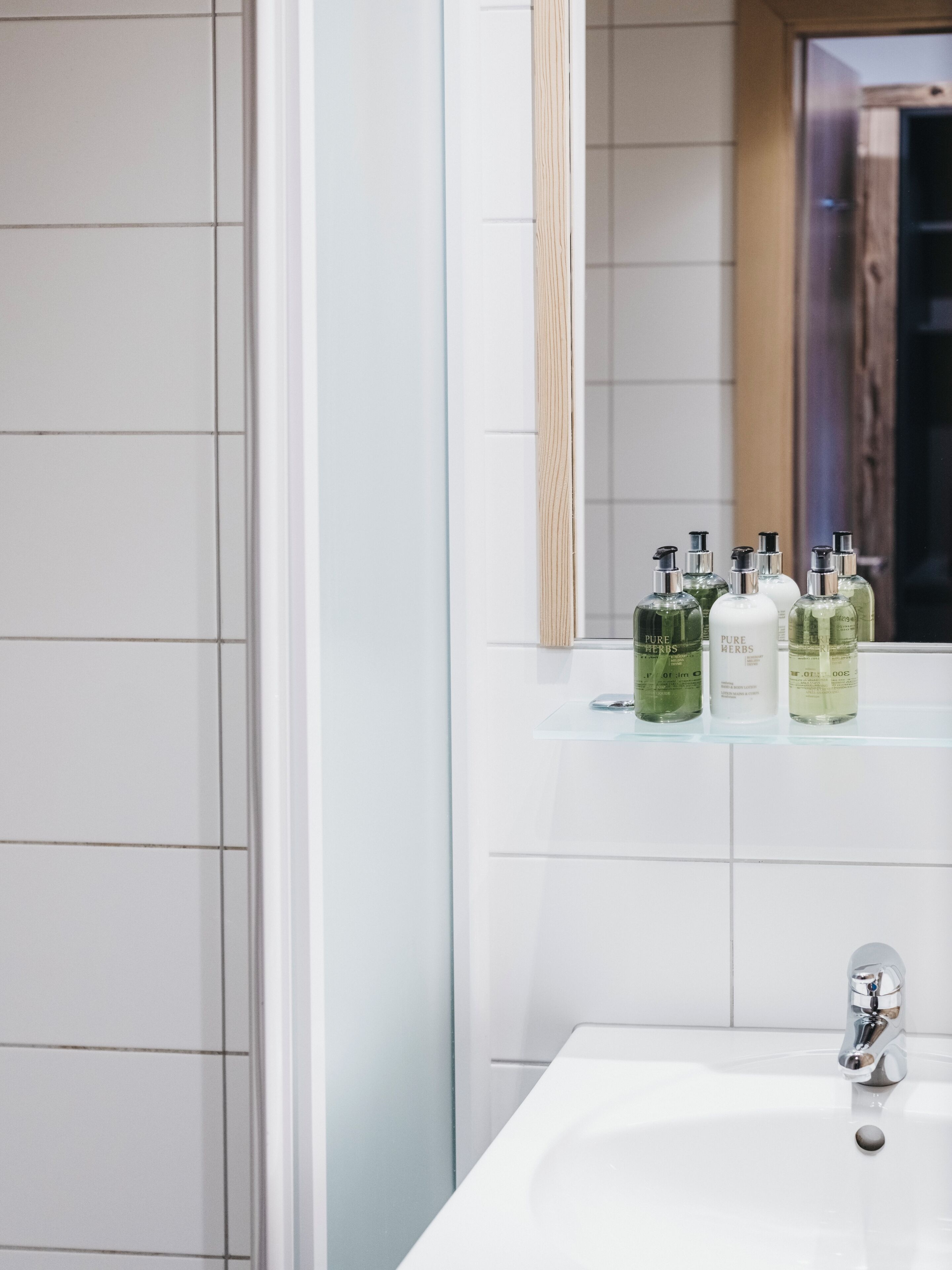 A bathroom with a white sink, a mirror, and shelves holding bottles of Pure Herbs products.
