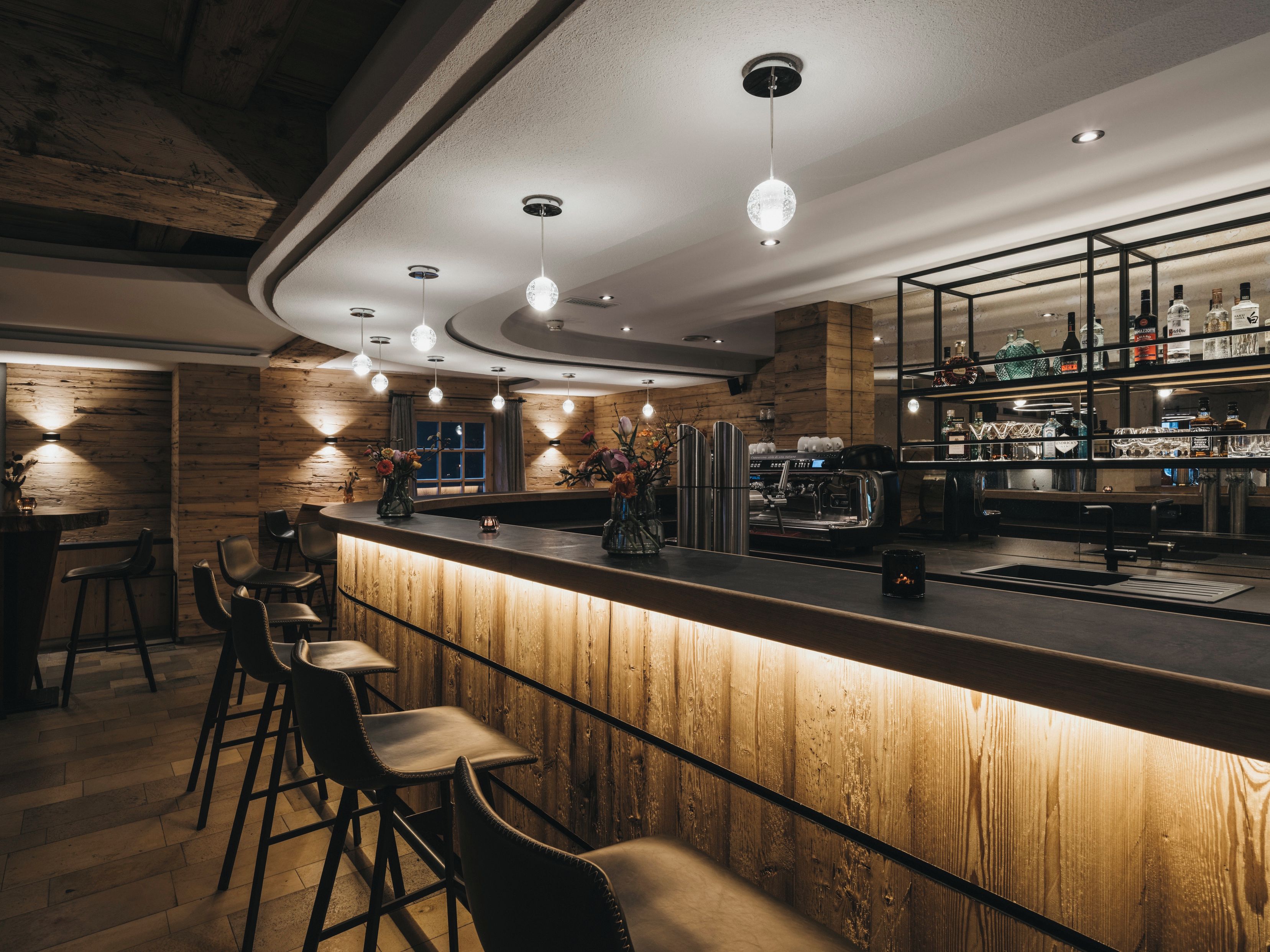 Eine Bar mit Holzelementen, Barhocker und freundlicher Beleuchtung.