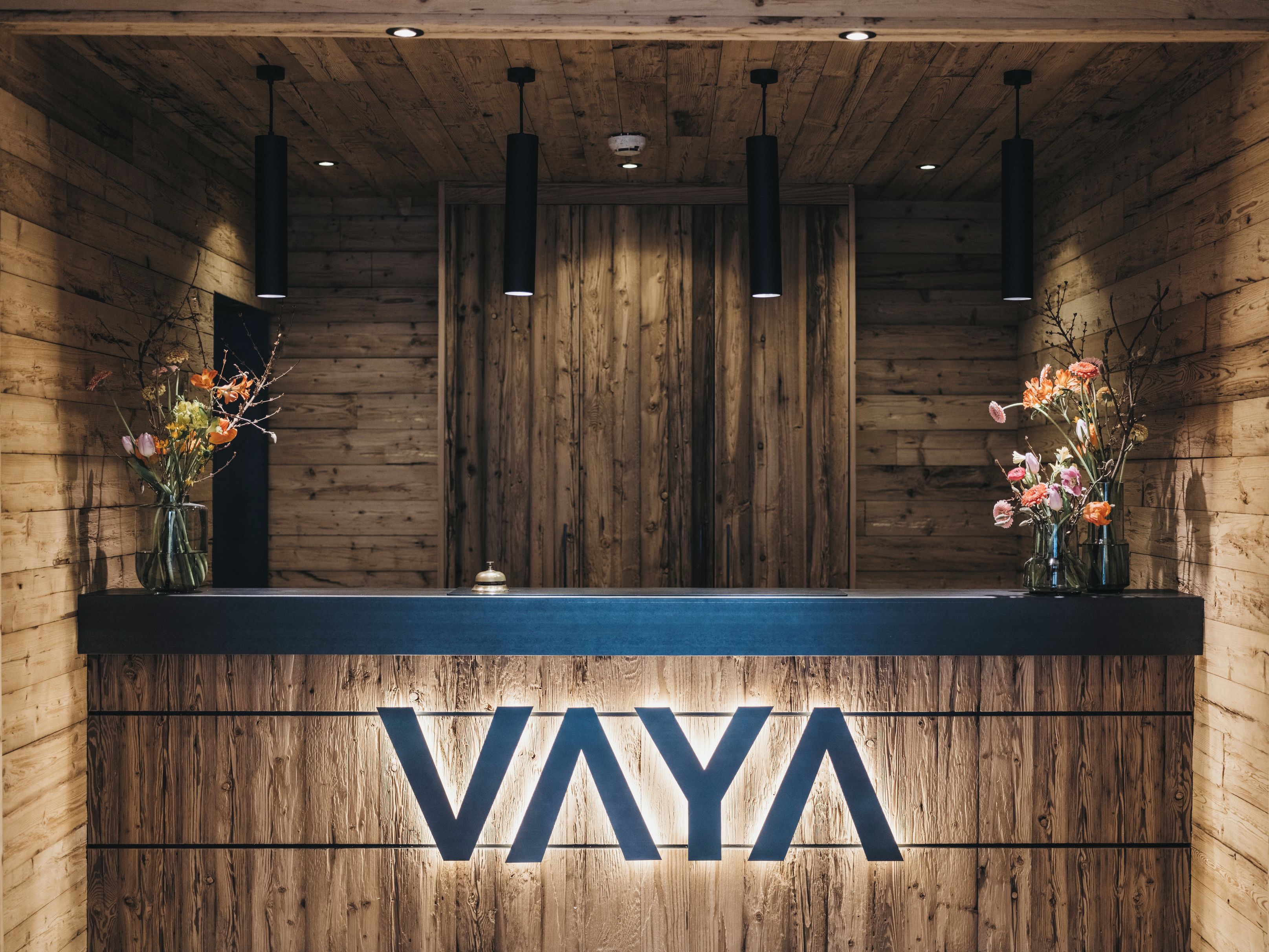 Ein Empfangstresen mit Holzverkleidung, auf dem der Name 'VAYA' in großen Buchstaben beleuchtet ist.