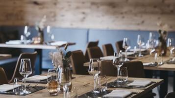 Un restaurant avec des tables en bois dressées pour le service, des lampes suspendues et un mur en briques rustiques en arrière-plan.