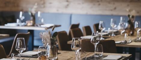 A restaurant with wooden tables set for dining, hanging pendant lights, and a rustic brick wall in the background.