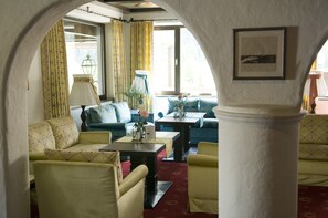 Un salon confortable avec un canapé, des fauteuils, une table basse et une lampe.