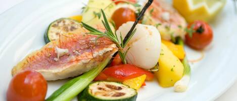 A plate of grilled fish with vegetables and a garnish.
